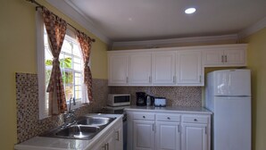 A kitchen with white cabinets, a microwave, a refrigerator, and a sink. - Apartment Soleil (Soufrière)