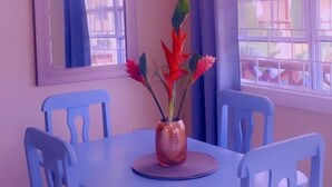 A dining area with a blue table and chairs, a vase with flowers, and a ceiling light fixture. - Apartment Soleil (Soufrière)