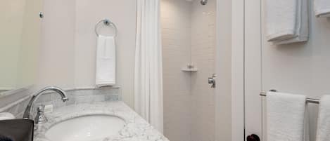 A modern bathroom with a marble sink, a glass shower enclosure, and white tiled walls.