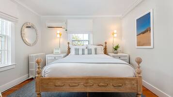 A bedroom with a wooden bed, white walls, a round mirror, and a window with a view of trees.