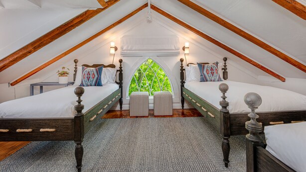 A bedroom with two beds, wooden beams, a window with a view, and bedside lamps. - Periwinkle Inn (Nantucket)