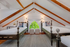 A bedroom with two beds, wooden beams, a window with a view, and bedside lamps.