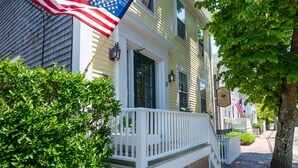 A yellow building with a white porch, an American flag, and a sign with a logo.