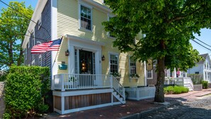 A yellow house with a white porch and a flag. - Periwinkle Inn (Nantucket)