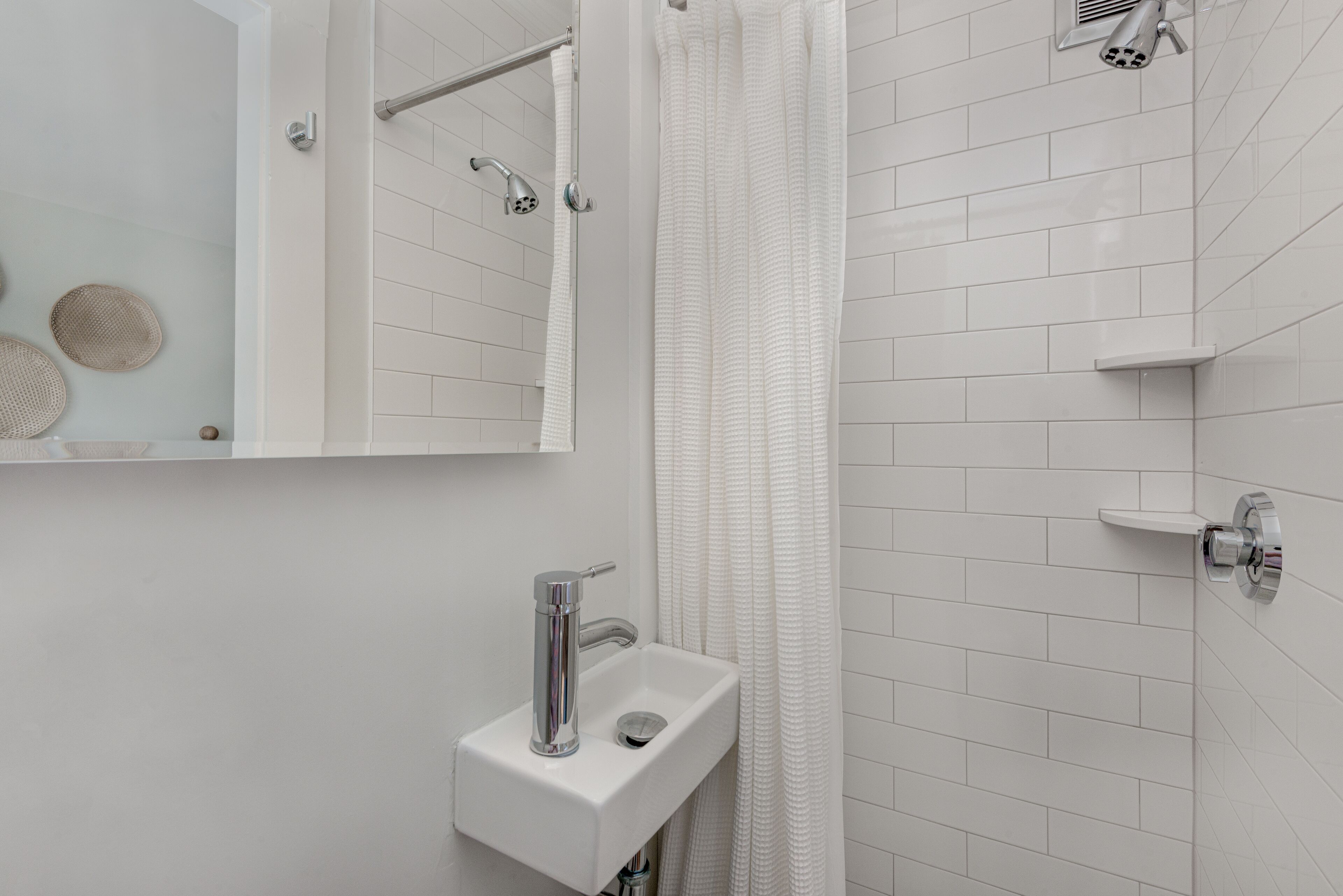 Un baño moderno con un lavamanos blanco, una ducha y un espejo.