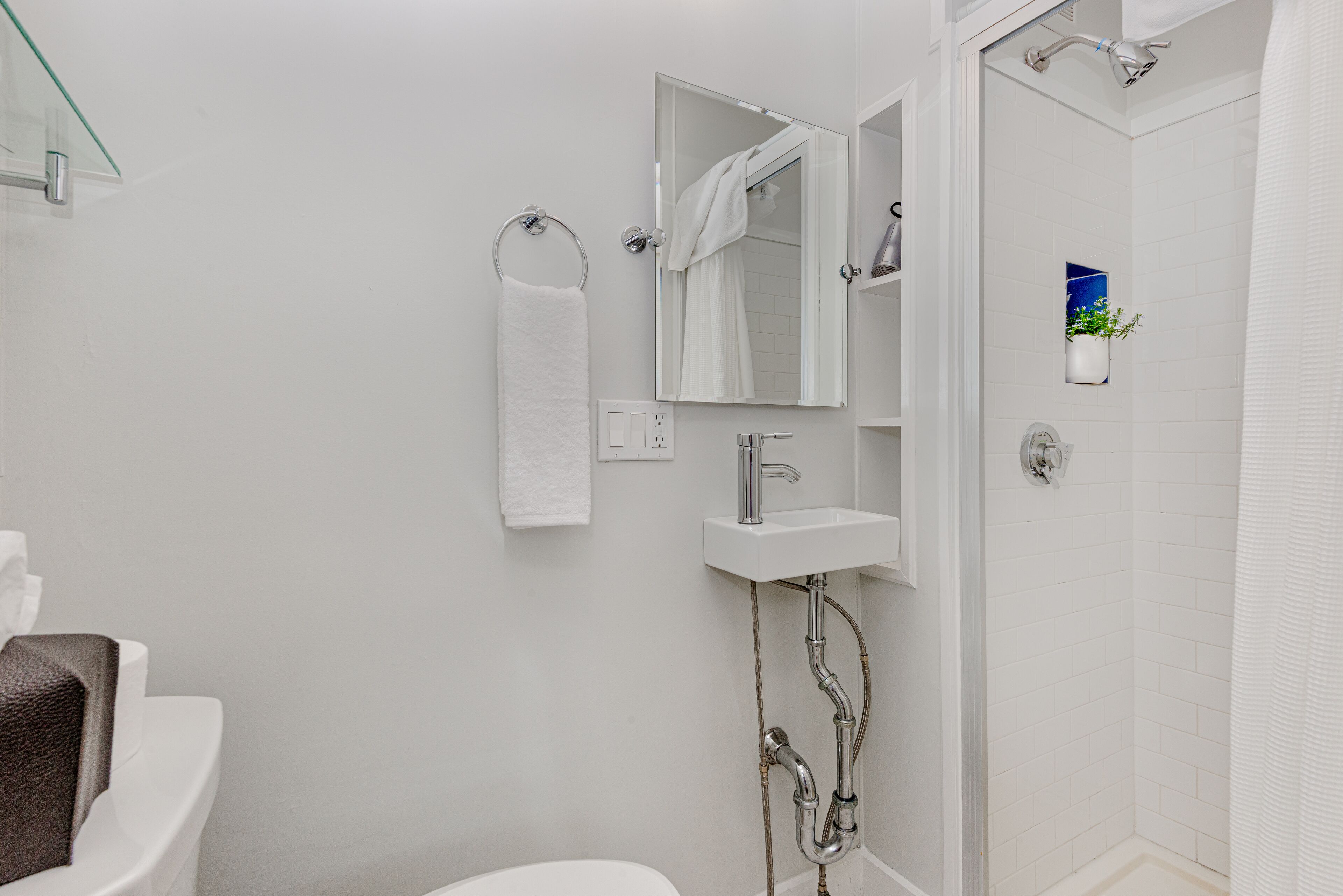 A modern bathroom with a white toilet, a glass shower enclosure, a white sink with a mirror above it, and a towel rack.
