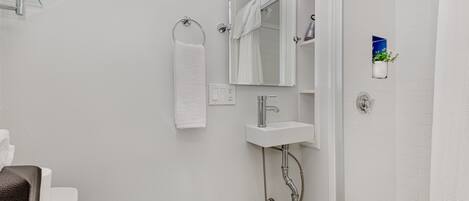 A modern bathroom with a white toilet, a glass shower enclosure, a white sink with a mirror above it, and a towel rack.