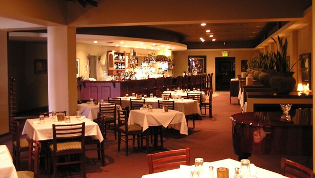 A restaurant with multiple tables and chairs, a bar area with shelves of bottles, and a warm interior lighting. - Tremont Inn on Main (Marshalltown)