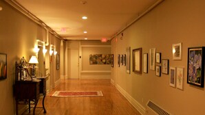 A hallway with wooden floors, wall-mounted lights, and framed artwork. - Tremont Inn on Main (Marshalltown)