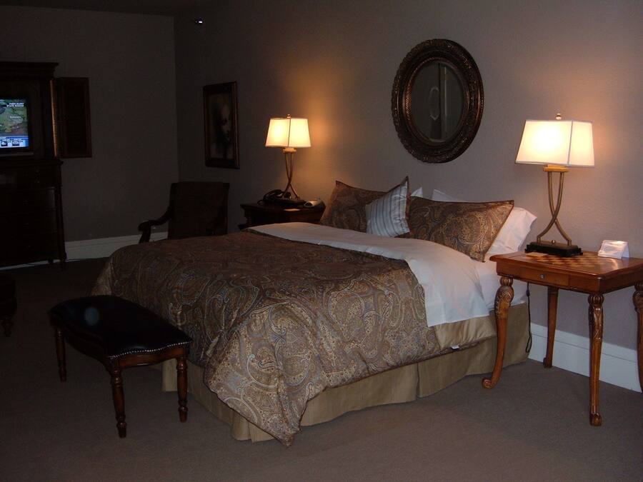 Une chambre d’hôtel avec un grand lit, deux lampes de chevet, une chaise, un bureau avec une lampe, une télévision et un miroir au mur.