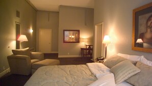 A hotel room with a bed, two chairs, a desk, and a painting on the wall. - Tremont Inn on Main (Marshalltown)