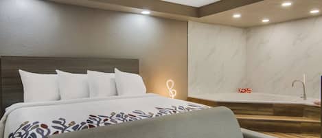 A modern hotel room with a large bed, a gray sofa, a marble wall, and a bathroom with a bathtub and a 'LOVE' sign.