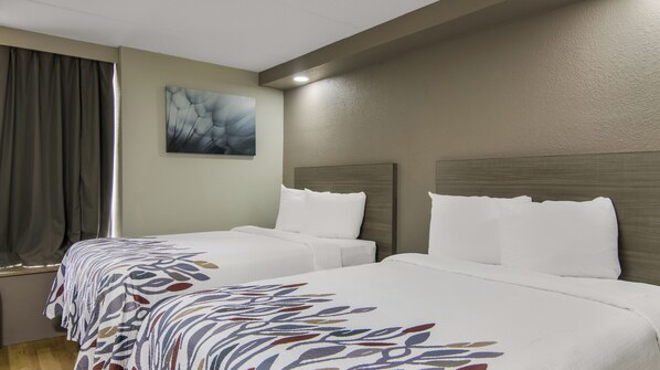 A hotel room with two beds, a large window with curtains, a painting on the wall, and a wooden headboard.