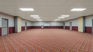 Une grande salle de conférence dotée d’un tapis à motifs, d’un écran de projection blanc et de portes le long des murs.