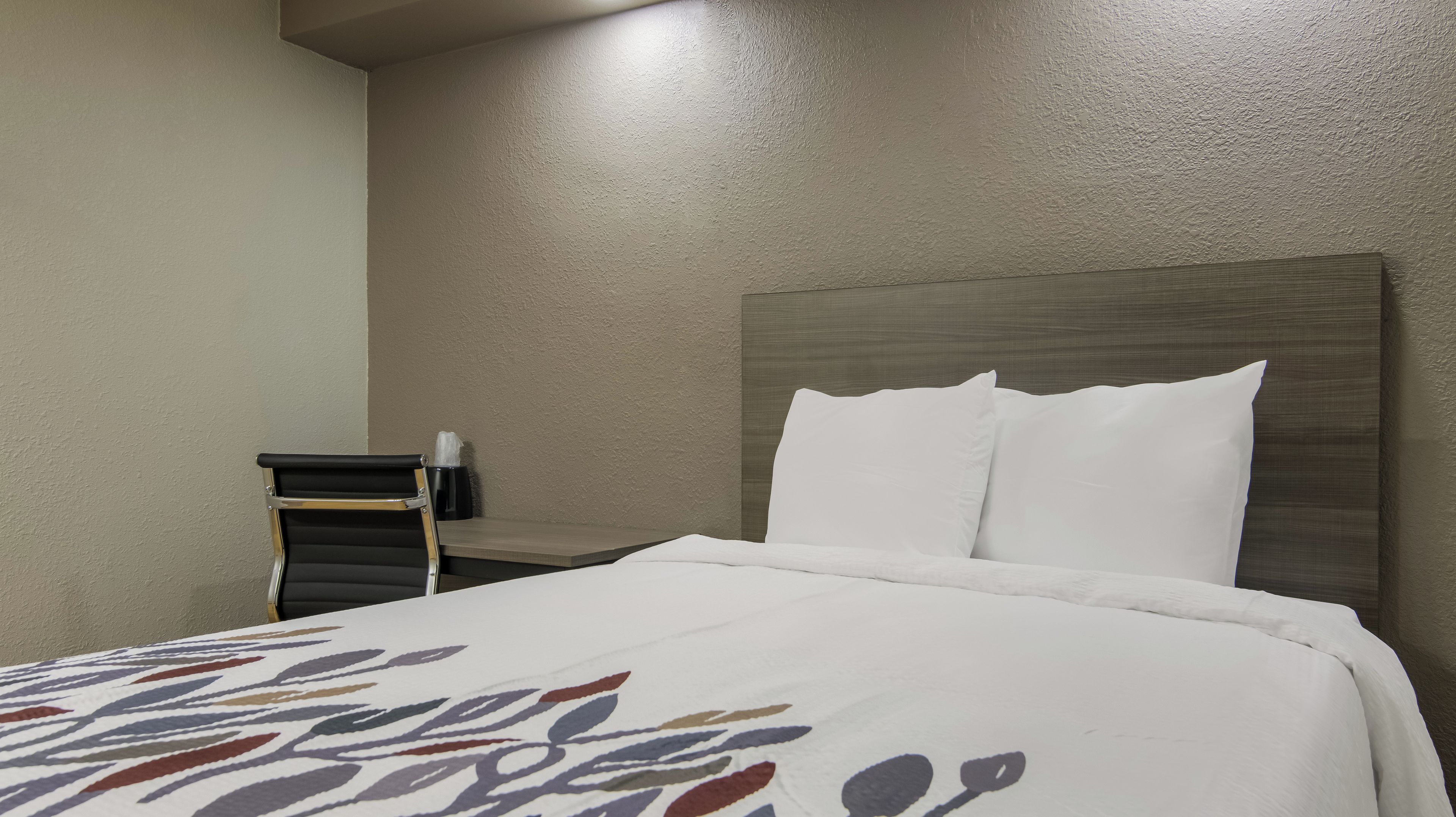 Una habitación de hotel con una cama, una silla y una mesita de noche.