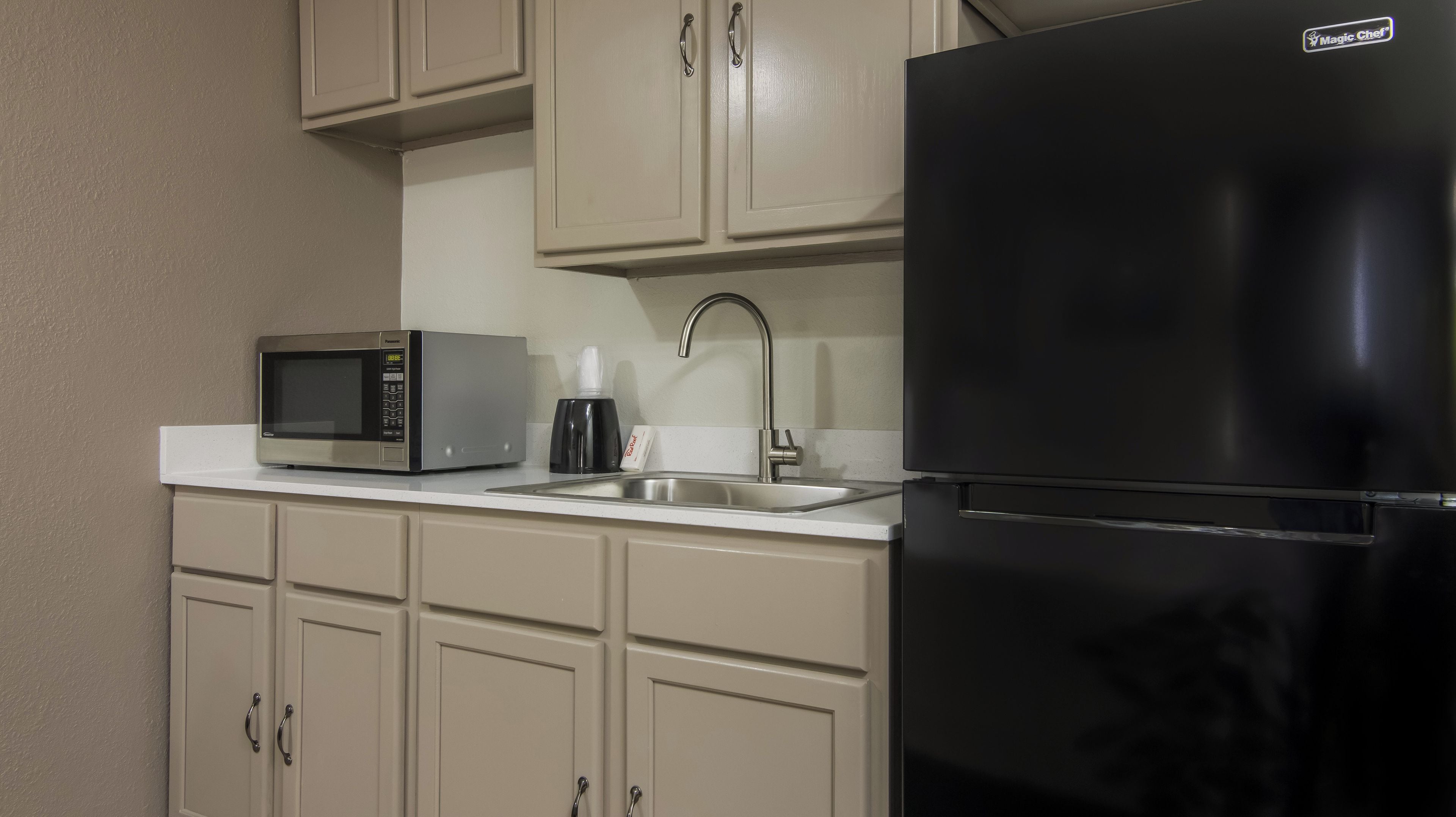 A kitchen with a black refrigerator, a microwave, a sink, and beige cabinets.