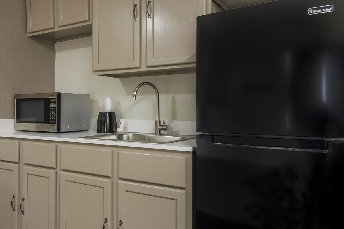 Une cuisine avec un réfrigérateur noir, un four à micro-ondes, un évier et des armoires de couleur beige.