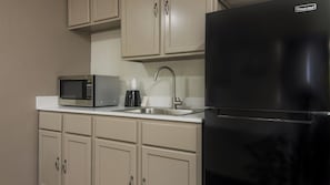 Une cuisine avec un réfrigérateur noir, un four à micro-ondes, un évier et des armoires de couleur beige.