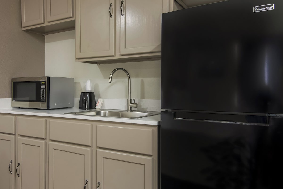 A kitchen with a black refrigerator, a microwave, a sink, and beige cabinets.