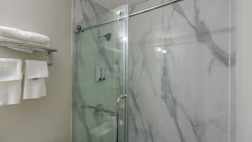 Ducha con paredes de vidrio, un perchero con toallas dobladas y un pasamanos.