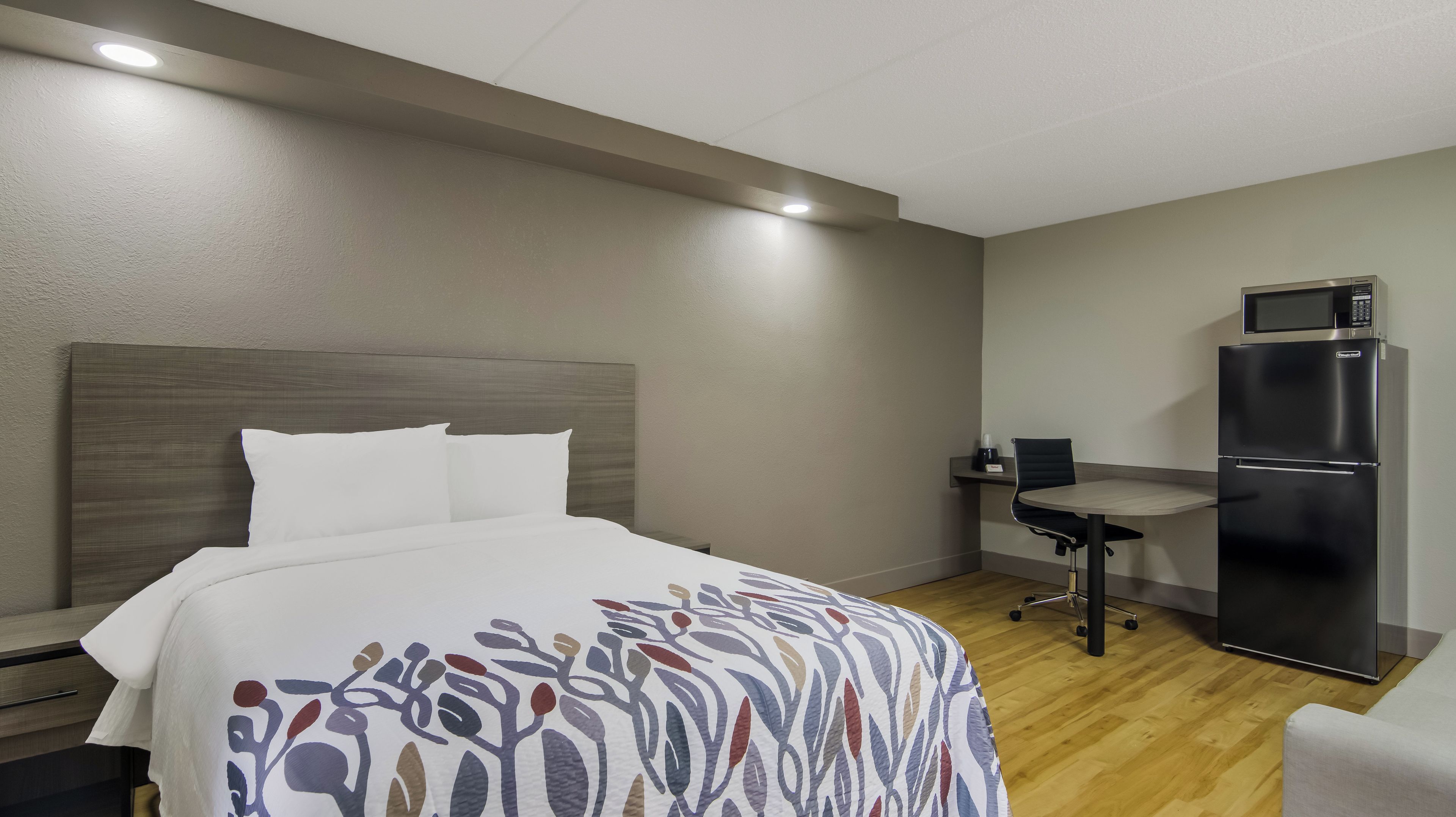 Una habitación de hotel con cama, escritorio, silla, refrigerador y microondas.