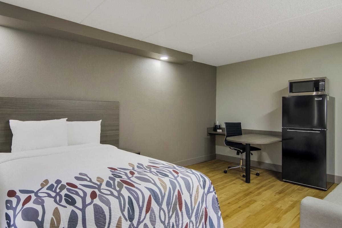 A hotel room with a bed, a desk, a chair, and a refrigerator.