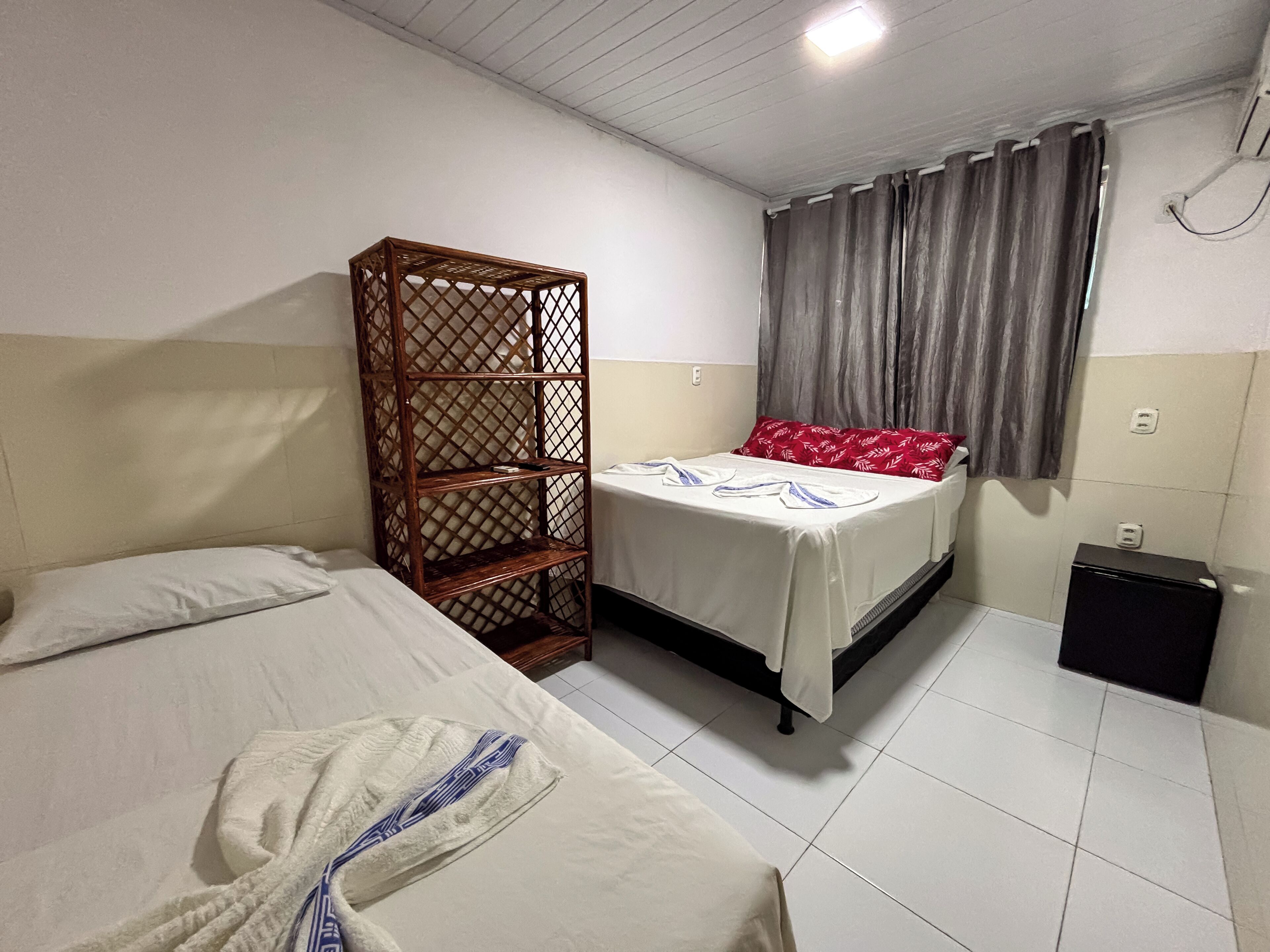 Habitación de hotel con cama, estante de madera, mesita pequeña y ventana con cortinas.
