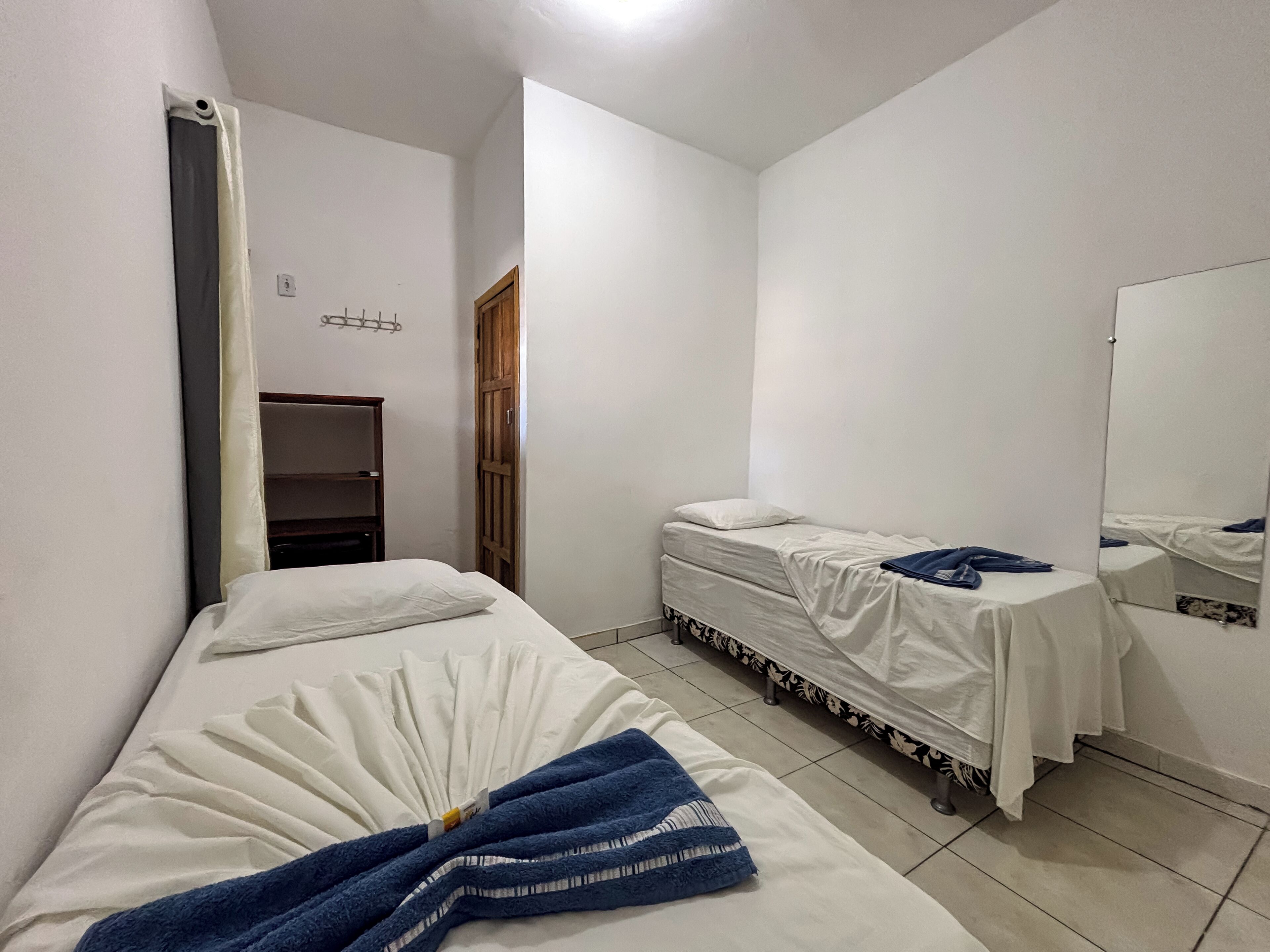 Habitación con una cama individual, un armario de madera, un espejo y una mesita de noche pequeña.