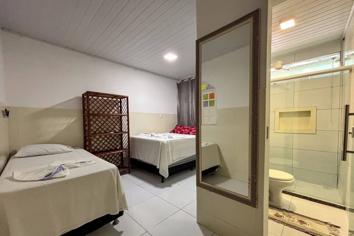 Habitación de hotel con dos camas, un armario, baño con ducha de vidrio y un espejo.