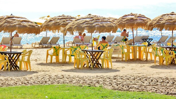 Un restaurante frente al mar con terraza, sombrillas de paja y vistas al océano.
