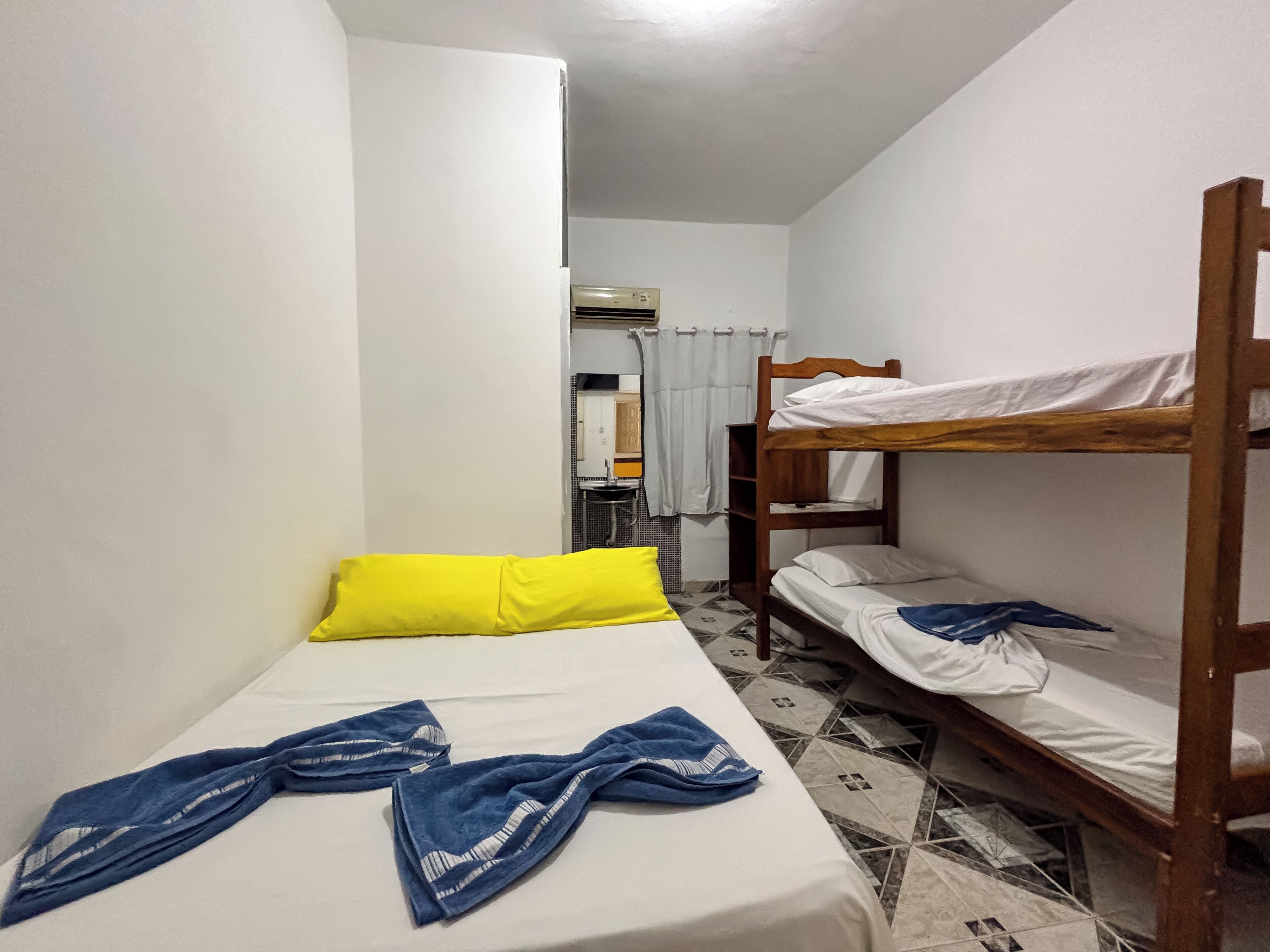 Quarto pequeno e compacto com uma cama de solteiro, uma cama individual com travesseiro amarelo e uma pequena mesa com pia.