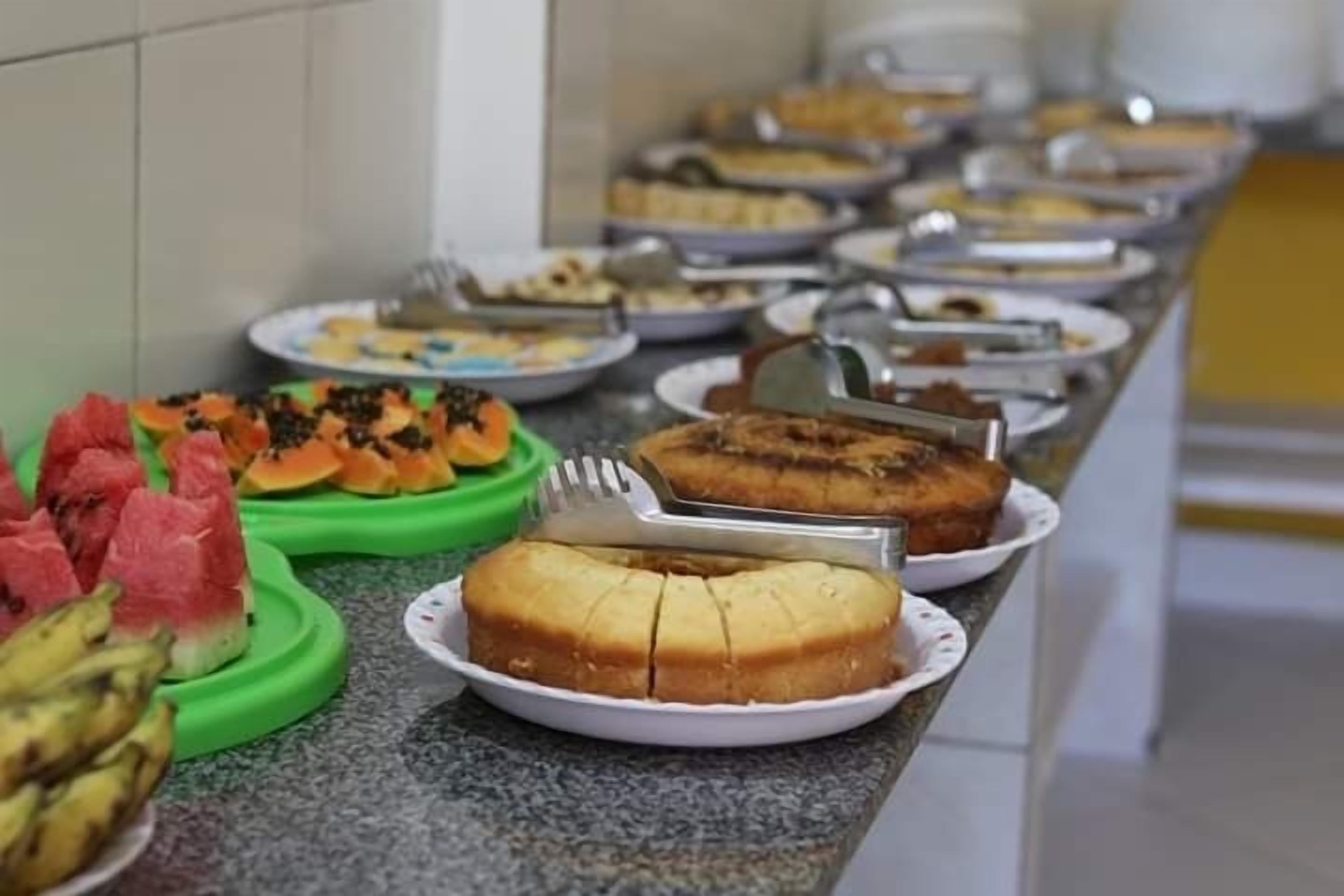 Buffet com diversos pratos, incluindo melancia, bolo e outros alimentos.