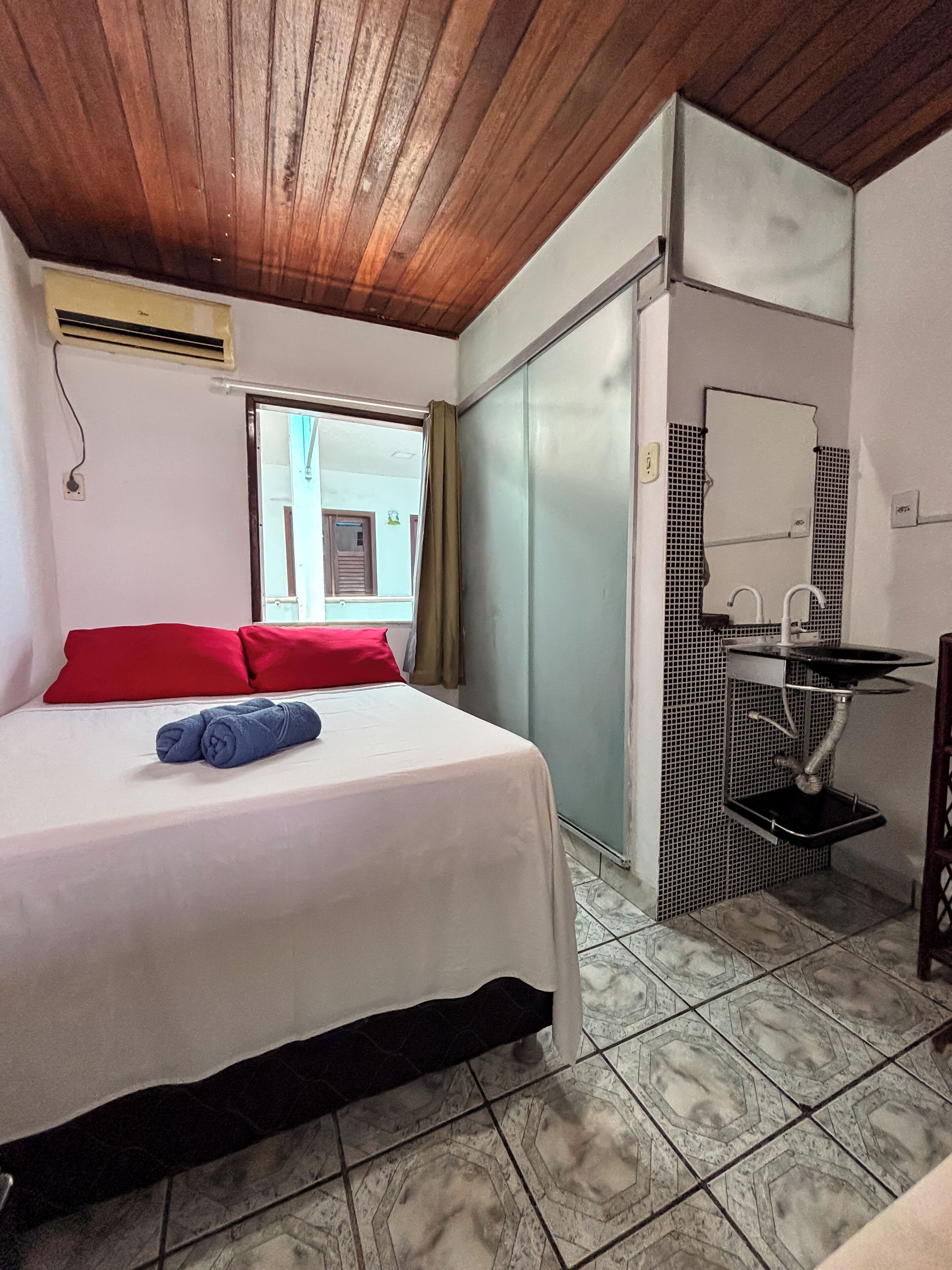 A hotel room with a bed, a bathroom with a sink and mirror, and a window with curtains.