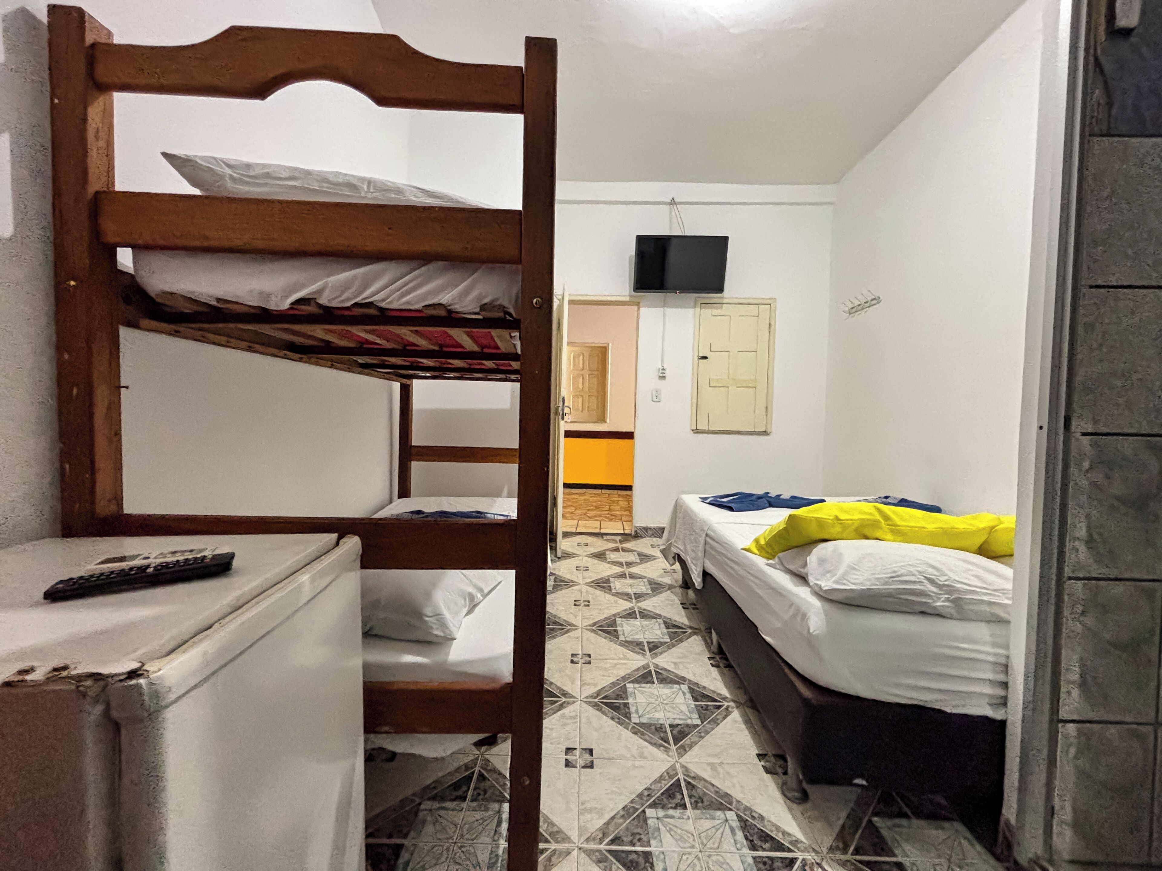 Une chambre de dortoir avec des lits superposés, un petit réfrigérateur, un téléviseur fixé au mur et un sol à motifs.