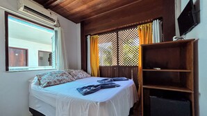 Un dormitorio con una cama, televisión, estante y ventana con cortinas.