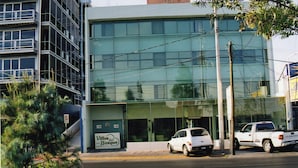 A modern hotel with a glass facade, a sign for 'Villas del Bosque', and two parked cars. - Hotel Villas del Bosque (Aguascalientes)