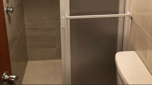 A small, enclosed shower area with a glass door, a toilet, and a tiled floor. - Hotel Villas del Bosque (Aguascalientes)