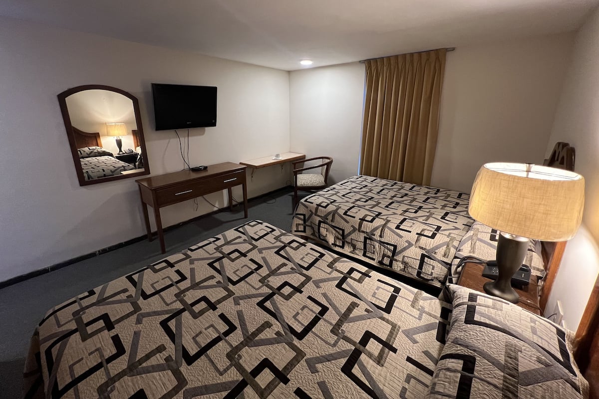 A hotel room with two beds, a desk, a chair, a TV, and a lamp.