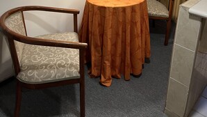 A small, round table with a patterned tablecloth, two upholstered chairs, a floor lamp, and a window with curtains. - Hotel Villas del Bosque (Aguascalientes)