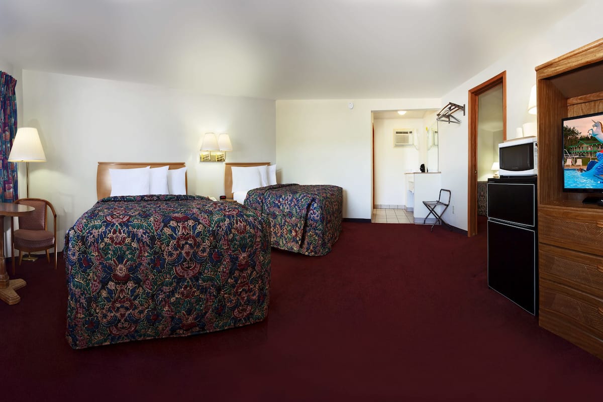 A hotel room with two beds, a desk, a chair, a TV, and a refrigerator.