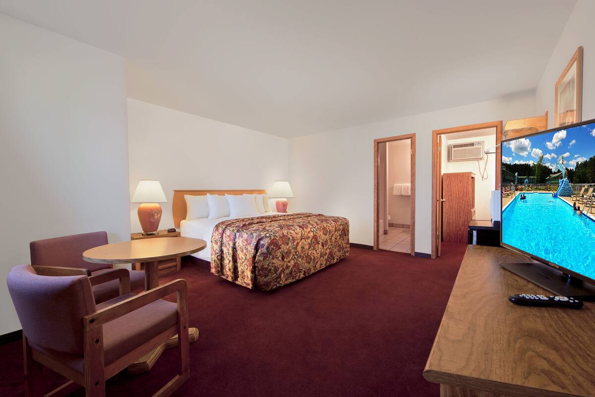 A hotel room with a bed, a desk with a TV, a chair, and a table with lamps.