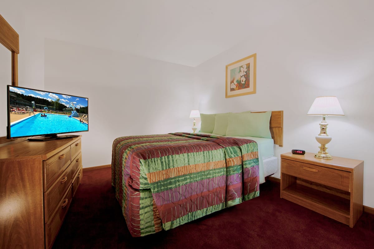 A hotel room with a bed, a TV on a dresser, a nightstand, and a lamp.