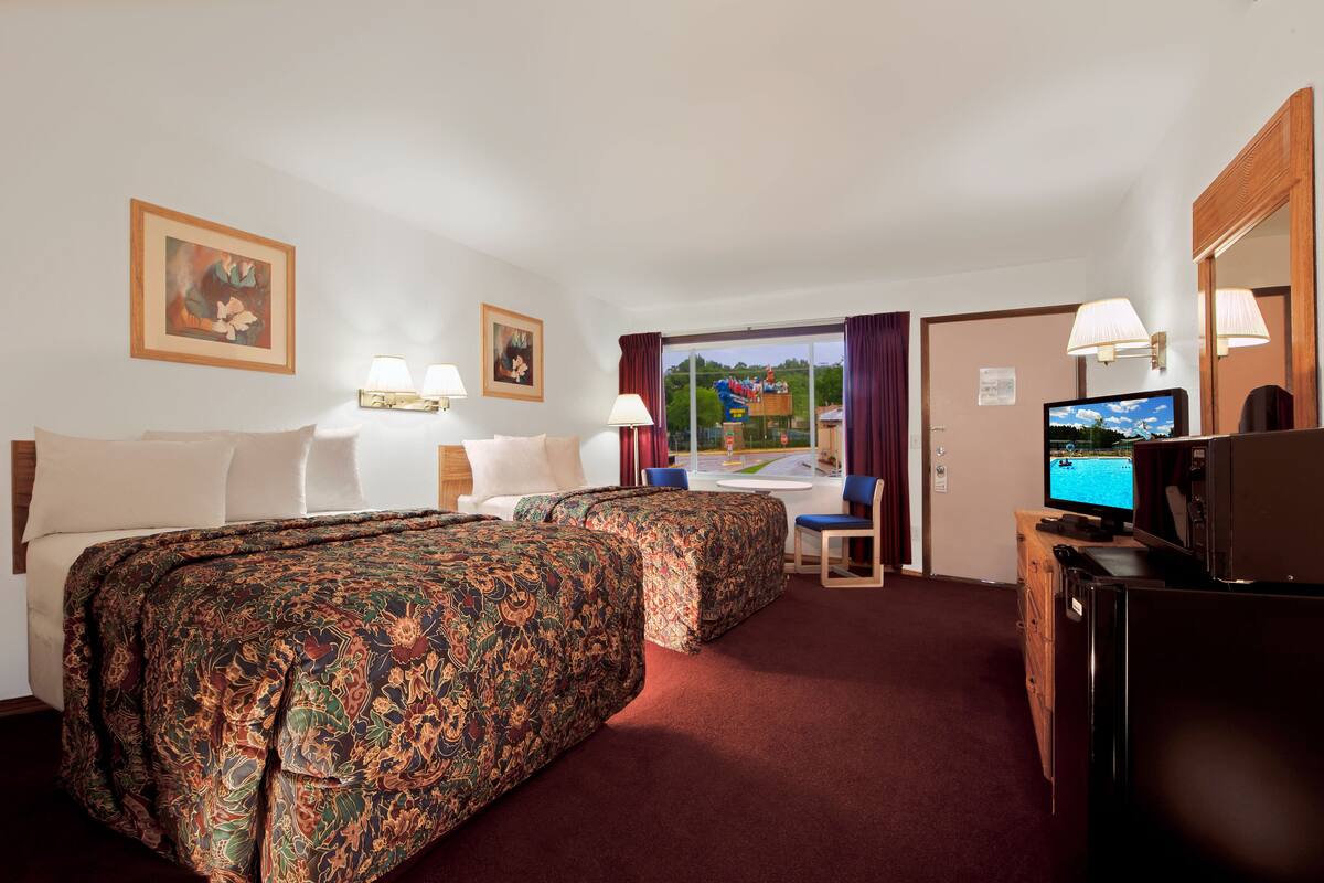 A hotel room with two beds, a desk with a chair, a television, and a large window with a view of the outdoors.
