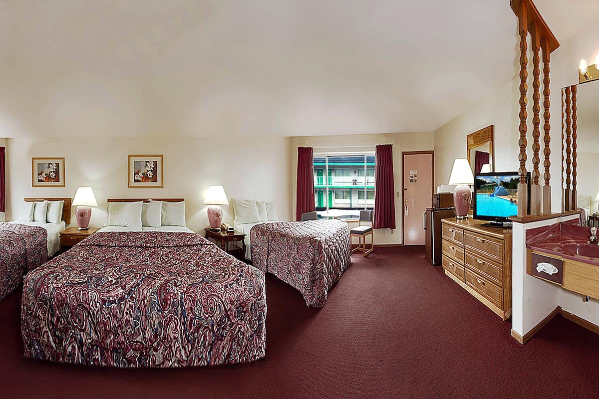 A hotel room with two beds, a desk, a dresser, a TV, and a window with curtains.