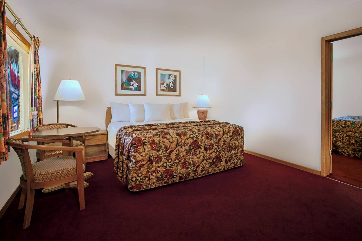 A hotel room with a bed, two bedside lamps, a chair, a desk, and a large mirror.