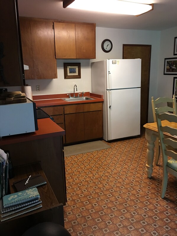 A compact kitchen with wooden cabinets, a white refrigerator, a sink, and a clock on the wall.