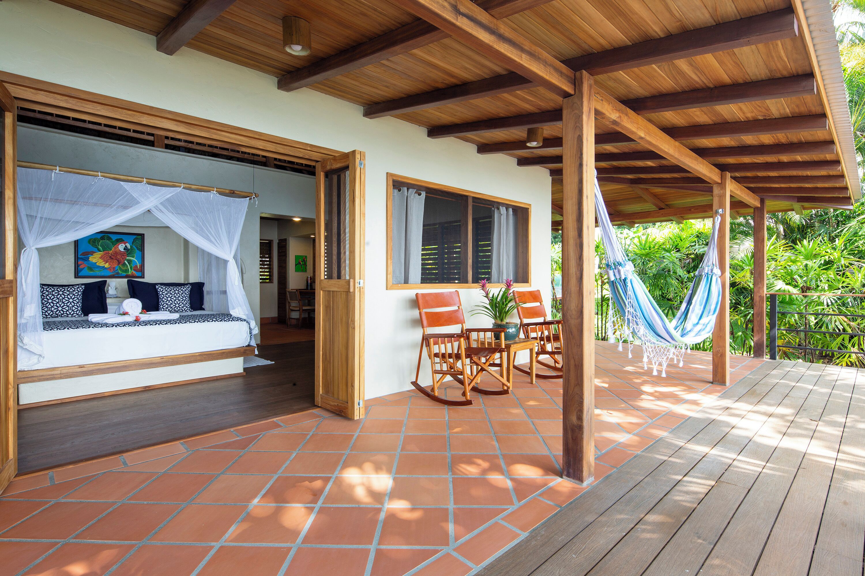 A covered outdoor seating area with a wooden deck, a bed with a mosquito net, and a hammock.