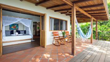 A covered outdoor seating area with a wooden deck, a bed with a mosquito net, and a hammock.