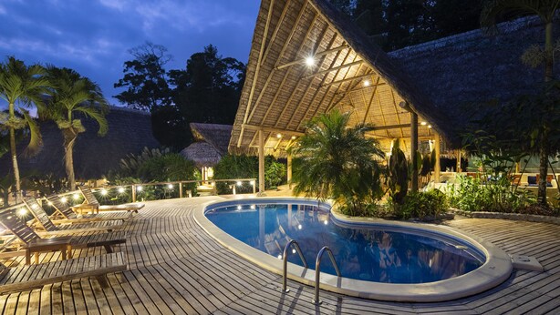 A pool area with lounge chairs and a thatched-roof structure.