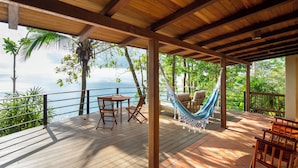 A wooden deck with a table and chairs, a hammock, and a view of the sea.